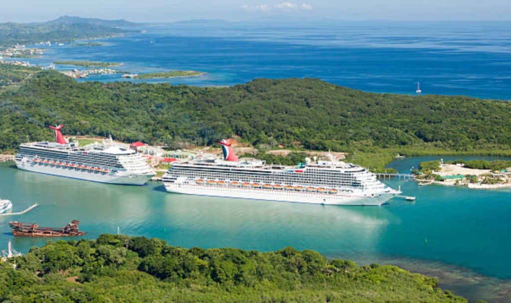 Aerial view of two cruise ships docked at Mahogany Bay cruise port in Roatan, Honduras, with turquoise Caribbean water and lush green tropical hills
